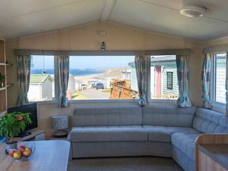 a living room with a grey sectional sofa and a view of the sea at Liskey Hill Caravan Park - Holiday Accommodation 20663 Perranporth
