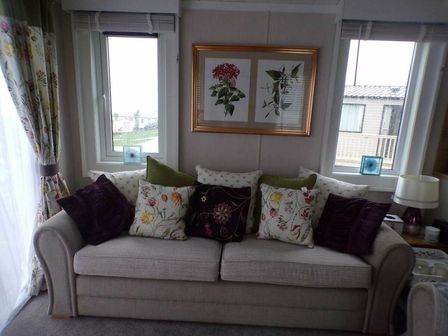 a sofa with patterned cushions and framed artwork in a room at Reighton Sands Holiday Park - Holiday Accommodation 2069, Filey