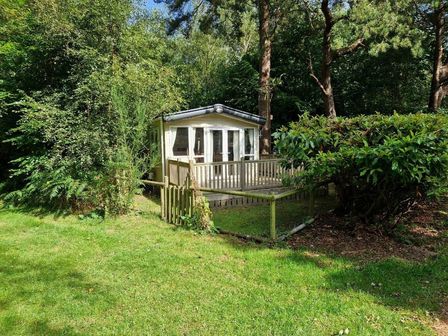 a cabin with a deck surrounded by grass and trees at Kelling Heath Holiday Park - Holiday Accommodation 20762 in Holt