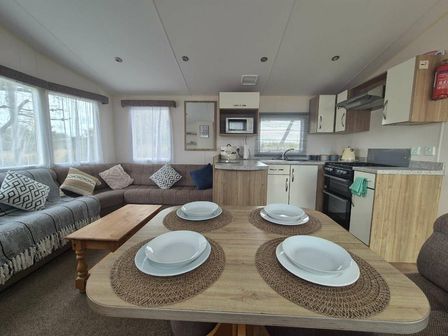 a dining table with plates and a kitchen area at Liskey Hill Caravan Park - Holiday Accommodation 20796, Perranporth