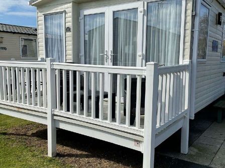 a deck area with white railing outside a mobile home at Presthaven Beach Resort - Holiday Accommodation 20917 in Gronant