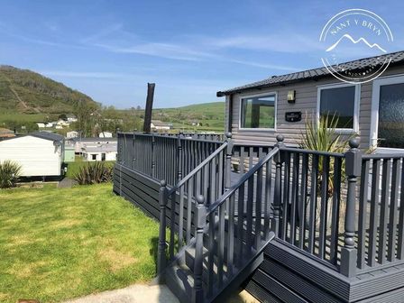 a deck with stairs outside a holiday home with green hills in the background at Clarach Bay Holiday Village - Holiday Accommodation 21107 Aberystwyth