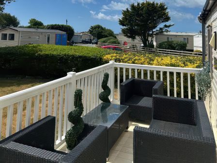 A terrace with black outdoor seating and a glass table at Greenacres Holiday Park - Holiday Accommodation 21168 Porthmadog