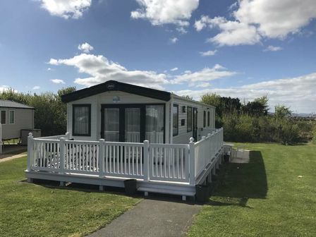 a mobile home with a white porch on a grassy area at Devon Cliffs Holiday Park - Holiday Accommodation 21246 Exmouth