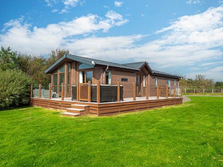 a wooden lodge with a deck and green lawn at Hafan y Mor Haven - Holiday Accommodation 21313 Pwllheli
