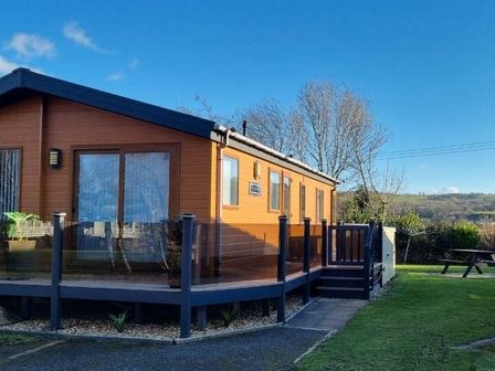 a wooden lodge with a deck and glass railing at Presthaven Beach Resort - Holiday Accommodation 21358 in Prestatyn