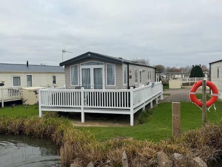 a holiday home with a porch by a pond at Manor Park Holiday Village - Holiday Accommodation 21362 Hunstanton