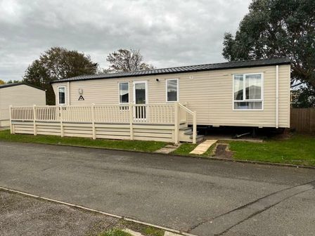 a mobile home on a street with a wooden deck and grassy area at Lyons Robin Hood - Holiday Accommodation 21484 Rhyl