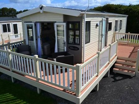 a mobile home with a deck and outdoor seating at Lizard Point Holiday Park - Holiday Accommodation 21549 in Helston