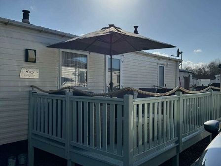 a mobile home with a deck and umbrella at Pinewoods Holiday Park - Holiday Accommodation 21638 Wells-next-the-Sea