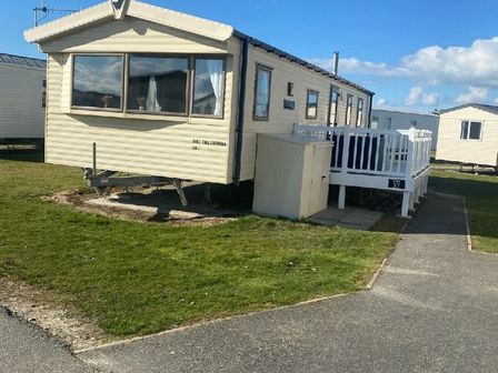 a caravan with a porch on a grassy area at Greenacres Holiday Park - Holiday Accommodation 21664 in Porthmadog