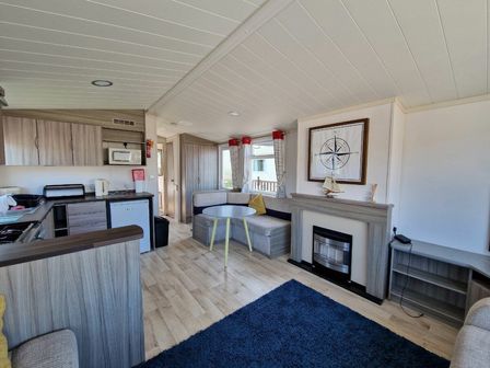 a living area with a sofa, coffee table, and kitchenette at Clarach Bay Holiday Village - Holiday Accommodation 21674, Aberystwyth