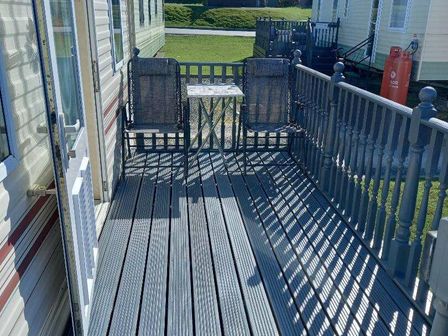 a deck with two chairs and a small table at Clarach Bay Holiday Village - Holiday Accommodation 21687, Aberystwyth