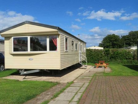 a caravan parked on a lawn with picnic benches at Skipsea Sands Holiday Park - Holiday Accommodation 21855 in Driffield