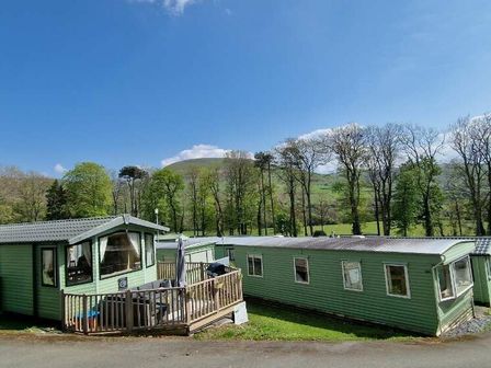 two green mobile homes in a grassy area with trees and hills at Woodlands Holiday Park - Holiday Accommodation 21859 Twywn