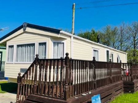a static caravan with a wooden deck in a recreational area at Clarach Bay Holiday Village - Holiday Accommodation 21967 Aberystwyth