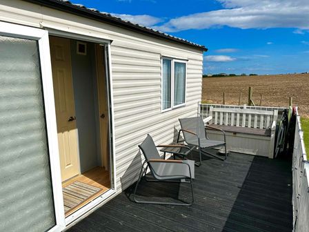 a deck area with two chairs and a table at Stoupe Cross Caravan Park - Holiday Accommodation 22028, Hawsker