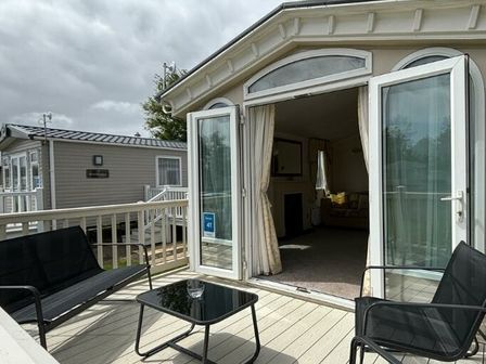 a deck area with chairs and a table leading into a caravan living area at Butlins Skegness - Holiday Accommodation 22071 in Ingoldmells
