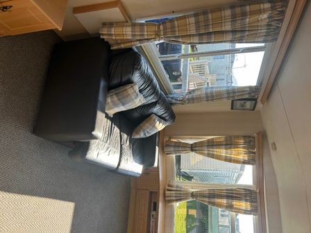a seating area with a black leather couch and checked curtains at Ty Gwyn Caravan Park - Holiday Accommodation 22138, Abergele