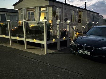 a caravan with a deck and outdoor lights next to a parked black car at Happy Days Caravan Park - Holiday Accommodation 22157 Towyn