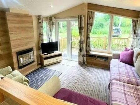 a living room with a sofa, armchair, television, and sliding doors at Kelling Heath Holiday Park - Holiday Accommodation 22251, Holt