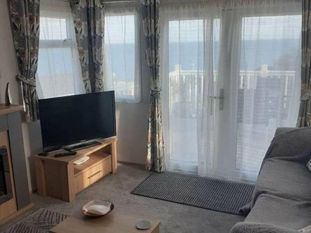 a living room with a television, a sofa, and curtains overlooking the sea at Waterside, Paignton - Holiday Accommodation 24