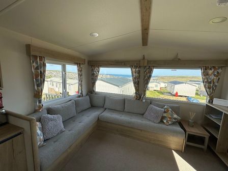 a seating area with a gray sectional sofa and a view of the coastline at Liskey Hill Caravan Park - Holiday Accommodation 3043 Perranporth
