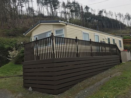 a mobile home with a deck in a wooded area at Clarach Bay Holiday Village - Holiday Accommodation 3416 Clarach