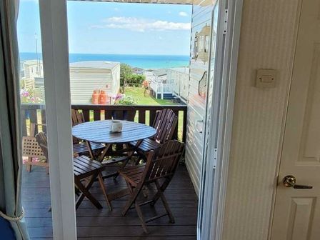 a balcony with a round wooden table and chairs overlooking the sea at Trimingham House Caravan Park - Holiday Accommodation 3496 Trimingham