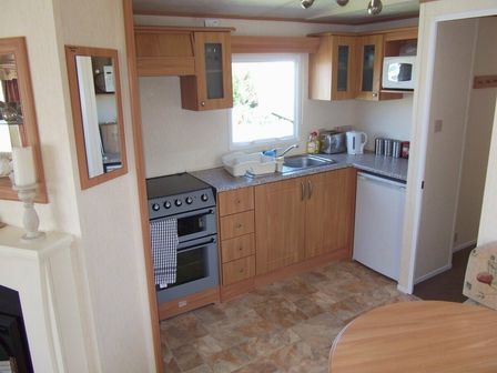 a kitchen area with wooden cabinets, an oven, a sink, and a small refrigerator at Seven Bays Park (Maribou) - Holiday Accommodation 3966 St Merryn