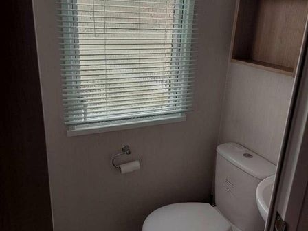 a bathroom with a toilet and a window with blinds at Reighton Sands Holiday Park - Holiday Accommodation 4398, Filey