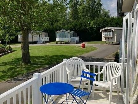 a balcony with blue table and chairs overlooking a lawn and holiday caravans at Hopton Holiday Village - Holiday Accommodation 453 Hopton, Great Yarmouth