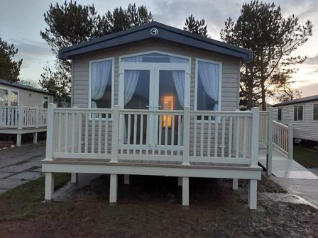 a holiday home with a wooden deck and large windows at Reighton Sands Holiday Park - Holiday Accommodation 6837, Filey