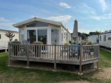 a holiday park caravan with a wooden deck and outdoor seating at Pinewoods Holiday Park - Holiday Accommodation 6988 Wells-next-the-sea
