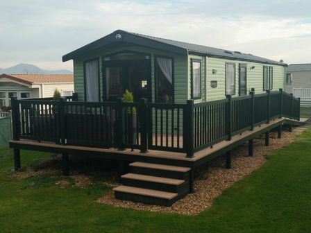 a holiday home with a green exterior and a deck at Hafan y Mor Haven - Holiday Accommodation 7021 Pwllheli