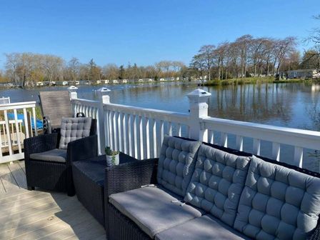 a seating area with wicker furniture overlooking a lake at Haggerston Castle - Holiday Accommodation 7202 in Berwick-Upon-Tweed