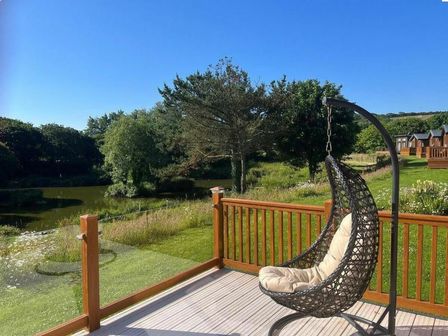 a hanging chair on a deck overlooking a pond and greenery at White Acres Holiday Park - Holiday Accommodation 7852 Newquay