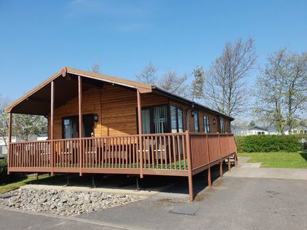 a wooden holiday lodge with a deck and grass area at Cala Gran Holiday Park - Holiday Accommodation 7934 Fleetwood