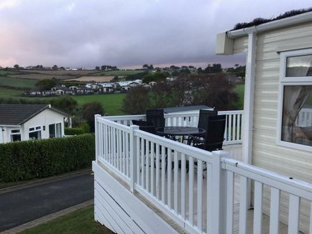 a deck with a table and chairs overlooking grassy areas at Praa Sands Holiday Park - Holiday Accommodation 8186, Praa Sands