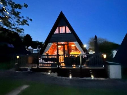 a triangular cabin with illuminated interior and a deck at Hafan y Mor Haven - Holiday Accommodation 8732 Pwllheli