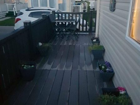 a wooden deck with potted plants and a table at Lido Beach Holiday Park - Holiday Accommodation 9040, Prestatyn