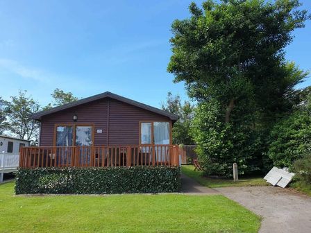 a wooden cabin with a front porch and greenery at Cala Gran Holiday Park - Holiday Accommodation 9426 in Fleetwood