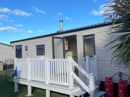 A caravan with a deck and gas cylinders at Green Farm Caravan Park - Holiday Accommodation 9807, Scratby, Great Yarmouth
