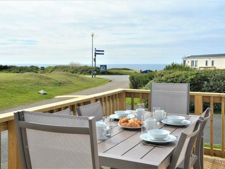 a dining table with white dishes and croissants on a deck overlooking the ocean at Perran Sands - Holiday Accommodation 9871 Perranporth