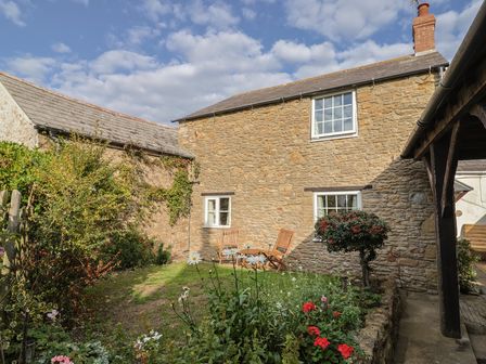 A garden with chairs and flowers at Vine Cottage in Burton Bradstock