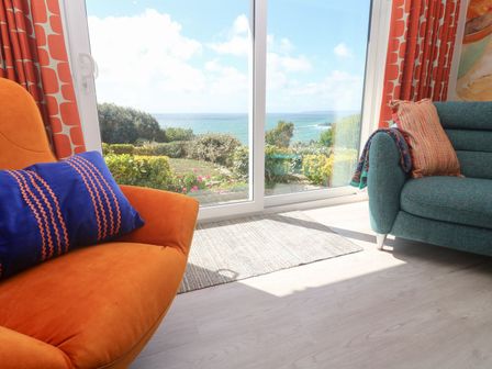 A living room with an orange armchair and a green sofa at Shearwater in Praa Sands
