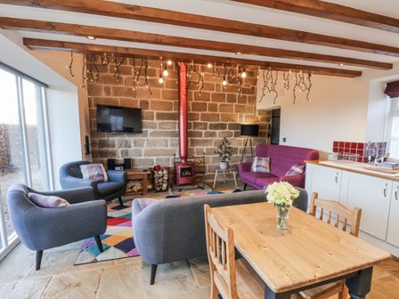 A living room with a sofa, armchairs, a wood stove and a dining table at Chestnut Barn Aislaby near Whitby