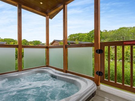A hot tub surrounded by wooden railing and glass panels at The Chesterton (Pet) in Kings Cliffe