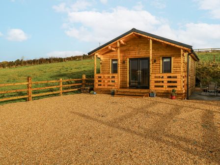 A log cabin with a gravel driveway and fence at Glenview Log Cabin in Ballycastle