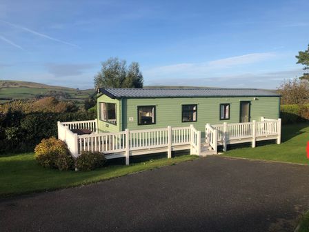 A caravan with decking and windows at Swanage Coastal Park Caravan in Swanage